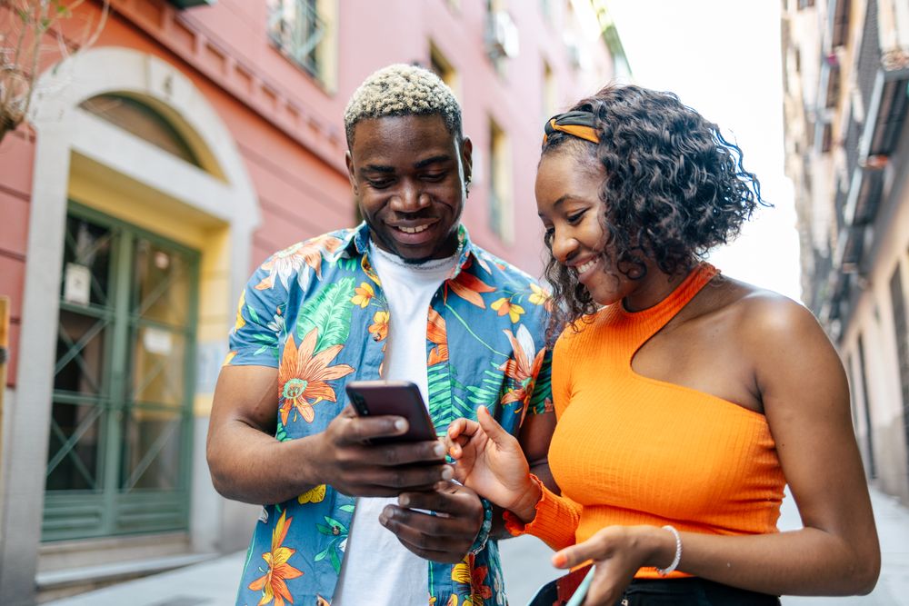Young Black friends using smartphone in the street