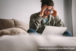 Stressed student studying at home with laptop on couch 0VrV30