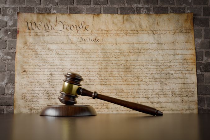 United States Constitution On Wall with Gavel Resting on Table in Front.