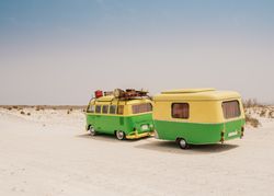 Colorful minibus with trailer parked on sandy shore in sunny day