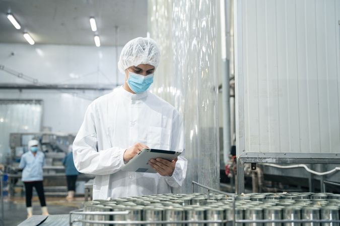 Researcher inspecting canned food processing on conveyor belt at fish factory
