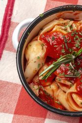 Bowl of delicious ravioli with tomato sauce and rosemary on table cloth