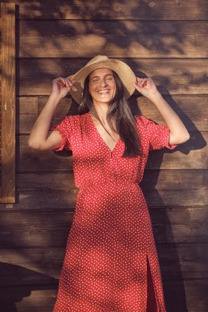 Happy woman in red dress and hat near wooden house