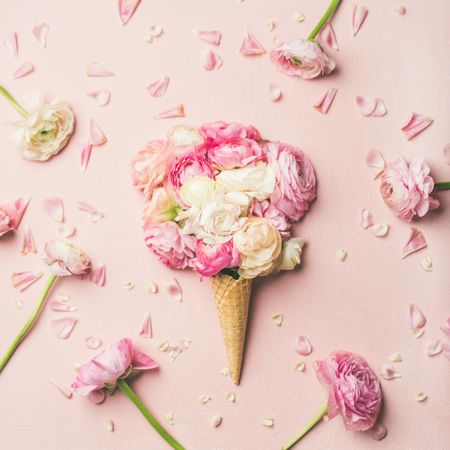 Waffle cone with pink buttercup flowers on a pink background with decorative flowers arranged