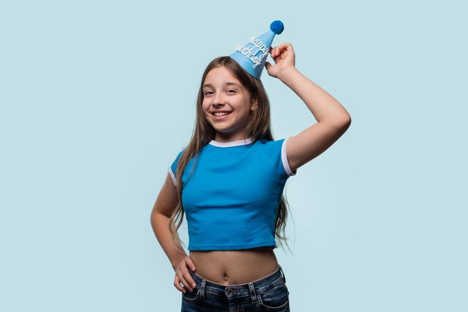Girl smiling and adjusting birthday hat, enjoying happy moment.