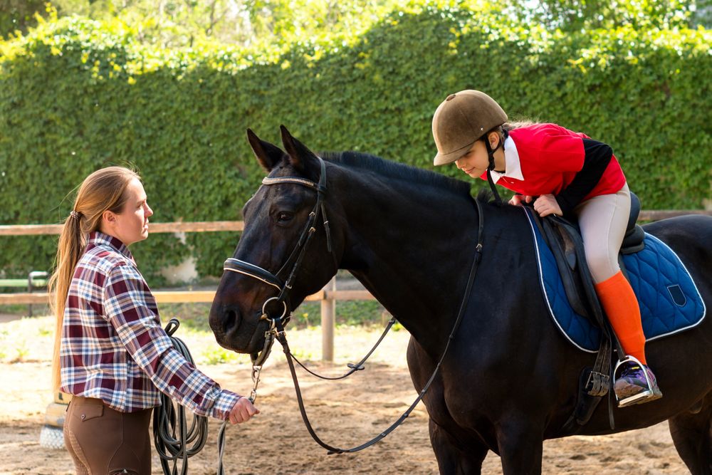 Young rider leans to touch horse during equestrian lesson.