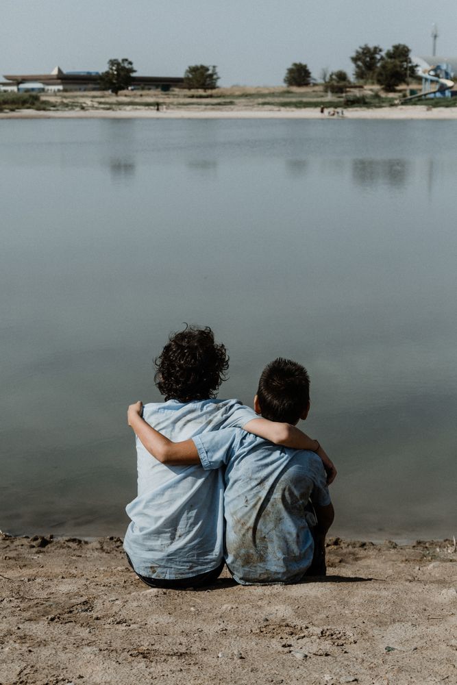 Unrecognizable kids sitting on ground by pond