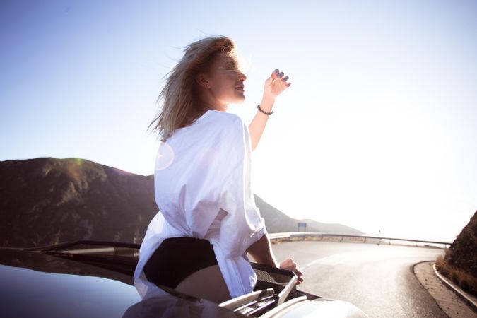 Rearview of curious woman standing out of sunroof on sunny day