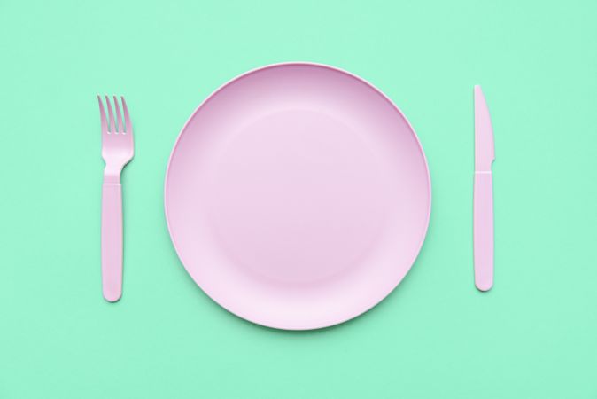 Pink plate and cutlery, above view, on a green table