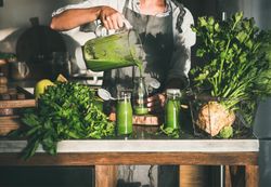 Woman pouring green smoothie into jars in kitchen