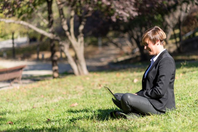 Side view of professional woman sitting cross legged in park with laptop