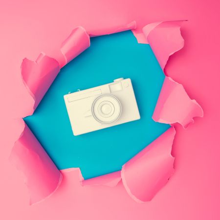 Torn pink paper revealing camera underneath on blue background