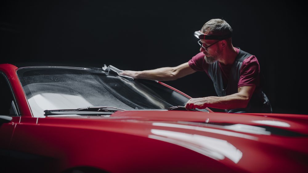 Portrait of a Car Detailer Spreading a Chemical Wax Solution for Polishing a Windshield and Protecting the Glass from Steaming Up During the Rain.