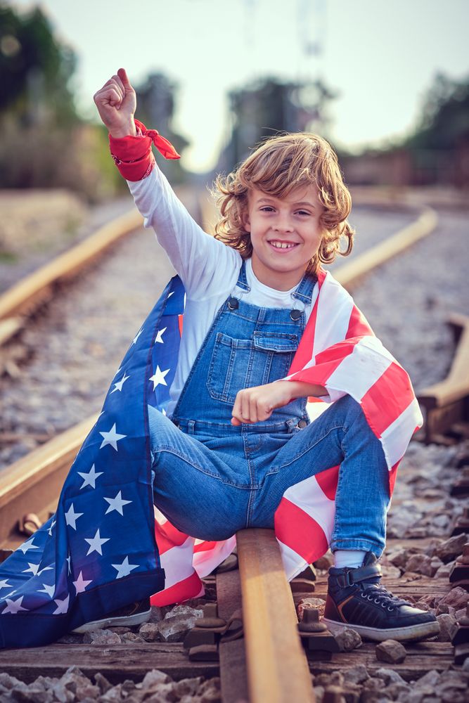 Cheerful boy with American flag sitting on railroad