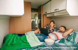 Male and female reclining on bed in motorhome with popcorn and digital tablet 5n2Y65