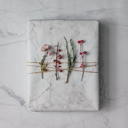 Marble wrapped present topped with winter foliage on marble background