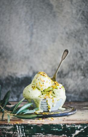 Bowl of melting pistachio ice cream with spoon and grey background