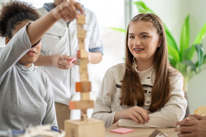 Girl in braces watches classmate building with wooden blocks