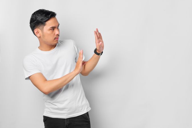 Asian male in grey studio gesturing “no” with both hands with copy space