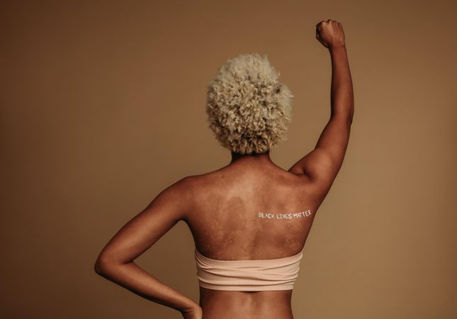 Rear view portrait of Black woman standing with arm raised on protest