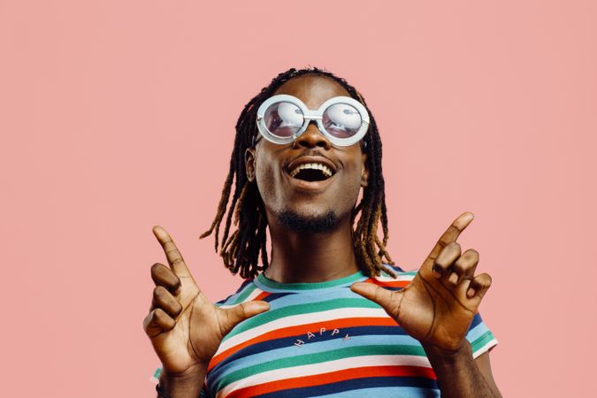 Very happy young man in striped shirt and big sunglasses, standing in front of a pink background