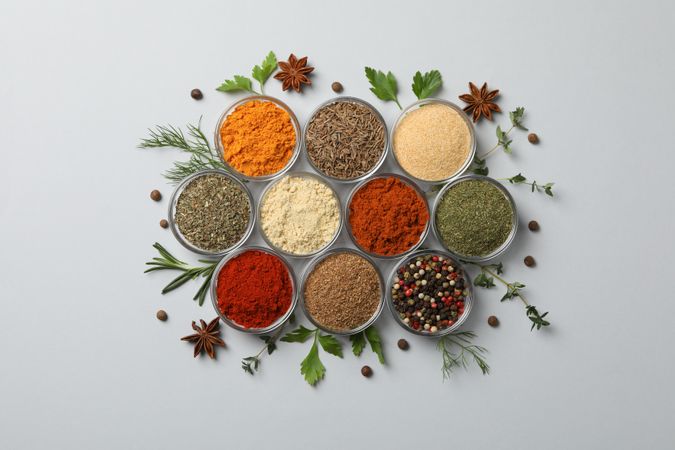 Top view of bowls of spice in neat rows surrounded with herbs