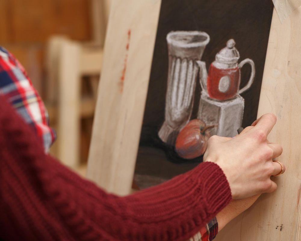 Hand of teacher guiding student as he draws a still life