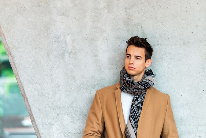 Bemused man wearing winter coat and scarf looking away against cement pillar