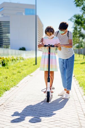 Girl on scooter with mother by her side helping her