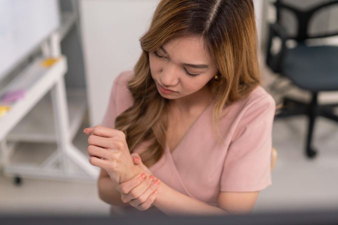 Asian woman holding her injured wrist while sitting at her desk