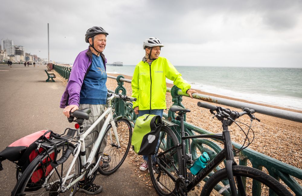 Two older people standing and talking with bikes looking towards the coast