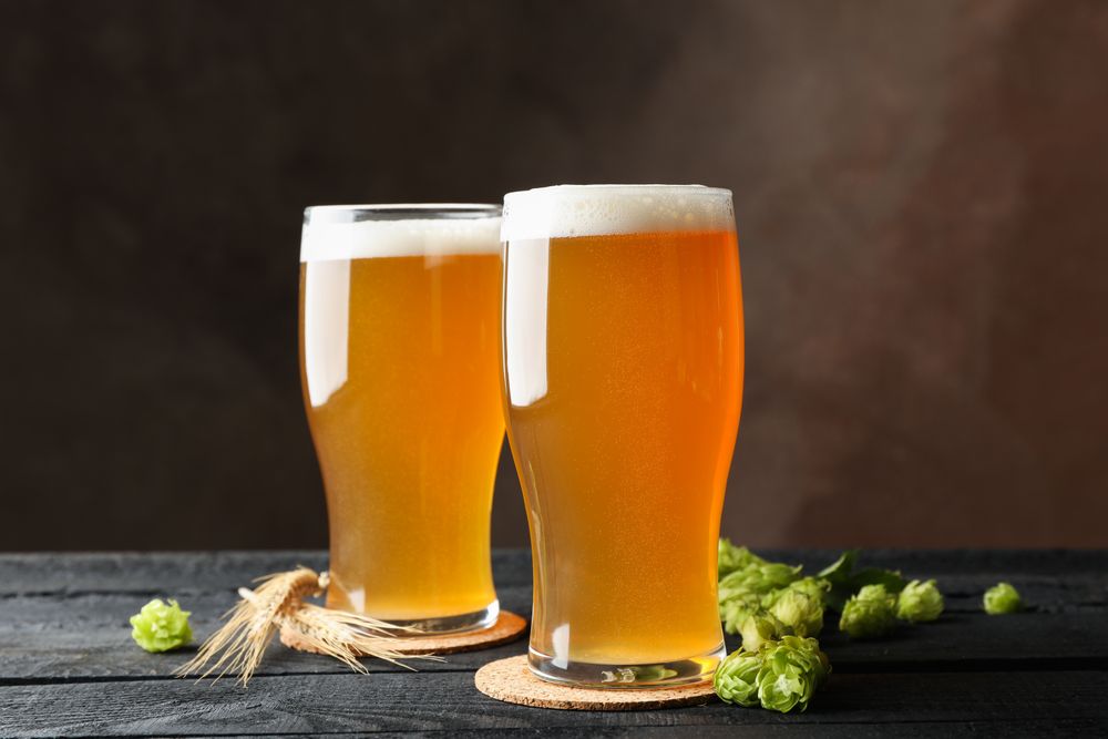 Glasses with beer, hop cones and spikelets on wooden table, space for text