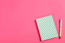 Copybook and pen on pink background, space for text