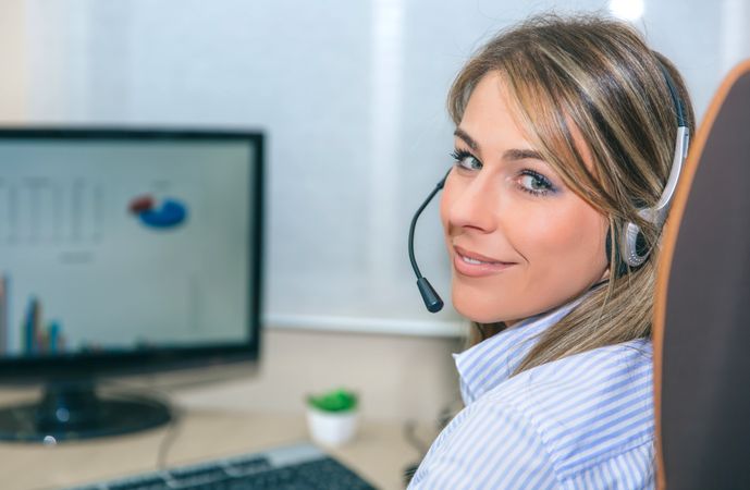 Smiling blonde woman working on graphs on computer in office