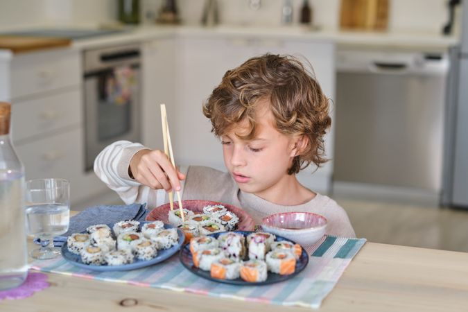 Adorable boy eating rolls in dining room at home