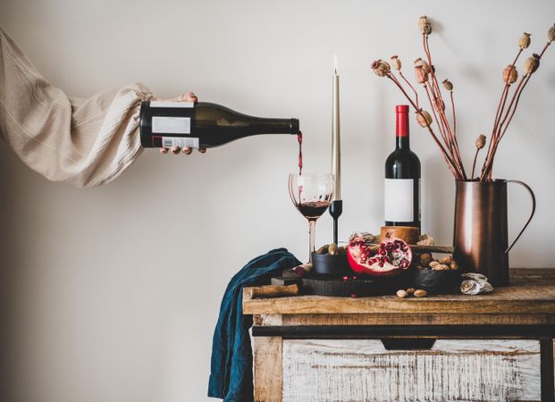 Rustic setting of woman pouring wine, cheese, long candles, with pomegranate, and dried poppies