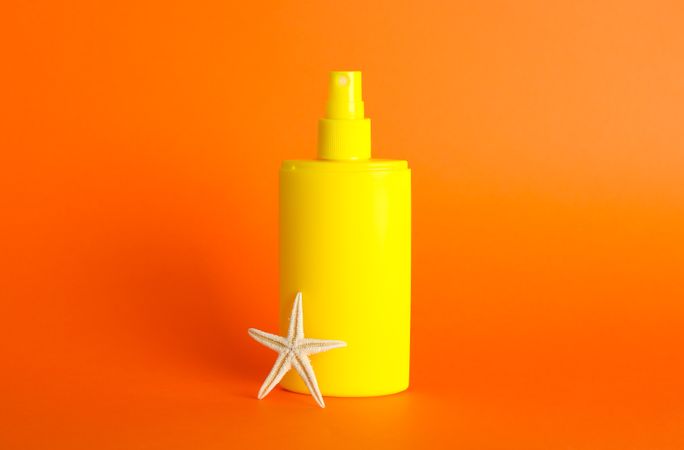 Sunscreen spray with starfish on color background, space for text