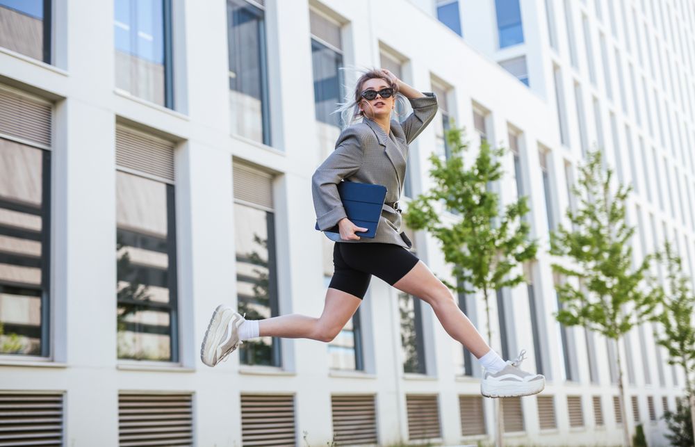 Woman with tablet in stylish suit jumping holding sunglasses
