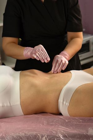 Beautician uses sculpting massage technique on woman’s abdomen.