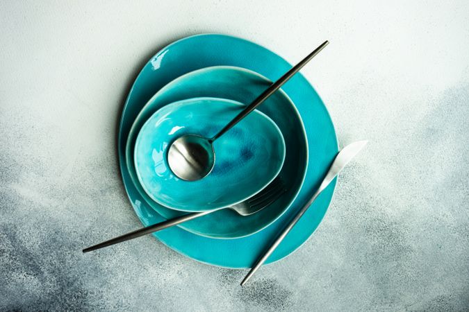 Top view of full teal table setting & silverware with on grey background
