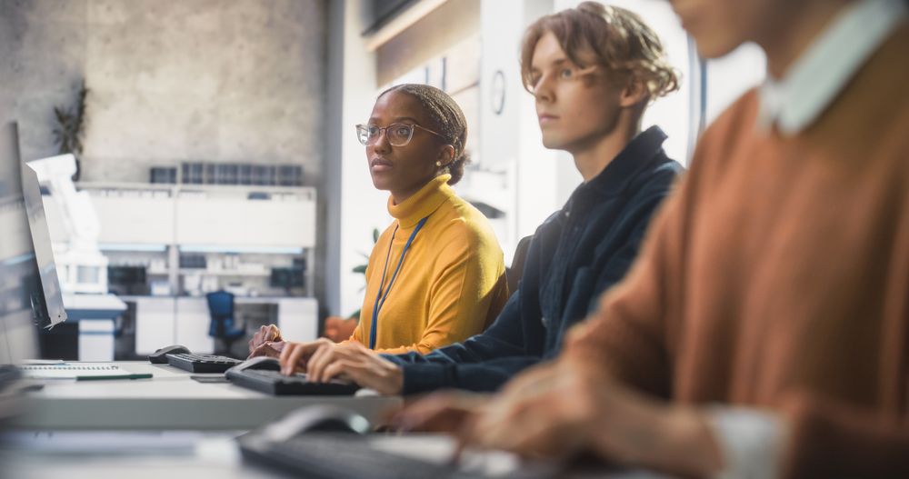 Diverse Multiethnic Group of Female and Male Students Sitting in College Room, Learning Computer Science.
