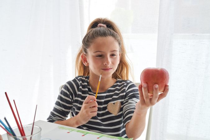 Girl with paintbrush looking at apple