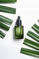 Green glass cosmetic bottle with pipete with green palm leaves.