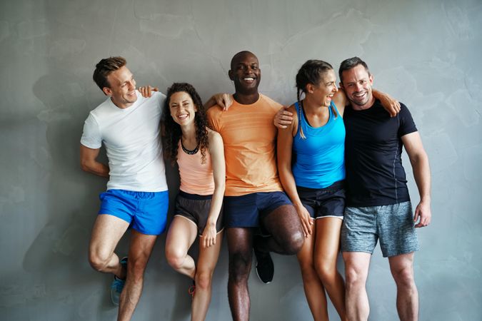 Multi-ethnic group of smiling people in workout gear leaning against a wall
