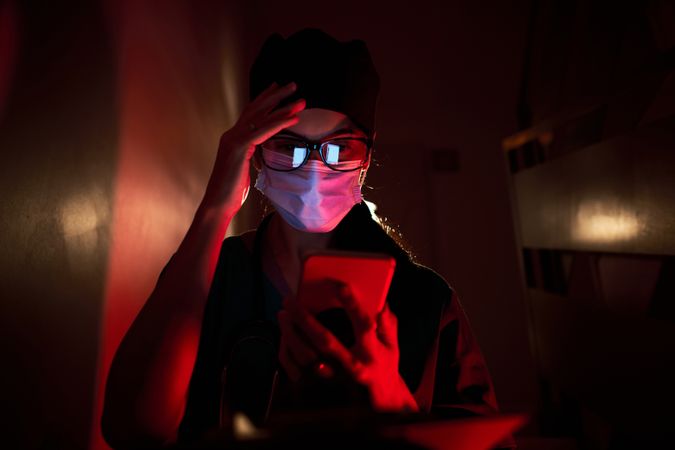 Confused doctor in mask looking at screen of cellphone