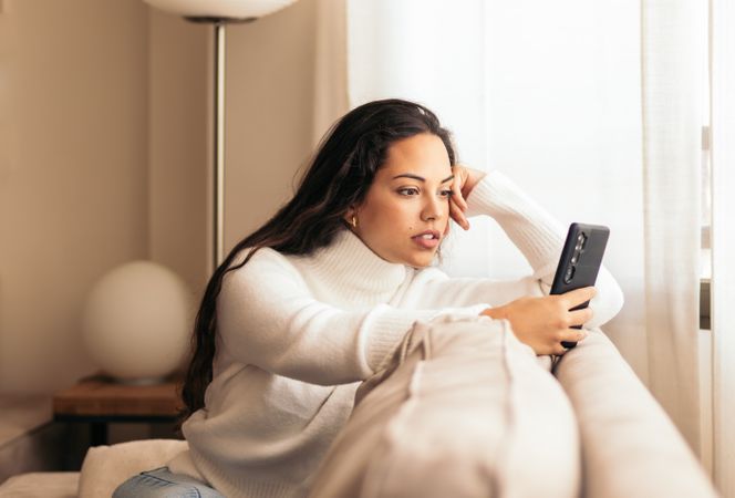 Connected at Home: Young Woman Sitting on Sofa Using Smartphone