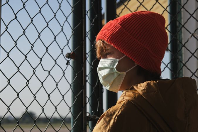 Anonymous teenager looking through chain link fence in sunlight