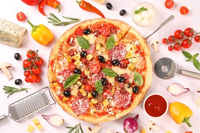 Flat lay. Tasty pizza, ingredients and kitchen supplies on plain background