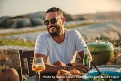Close up of a smiling man in sunglasses sitting at a table with food and drinks bGqMV5