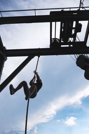 Anonymous man climbing rope in outdoor gym